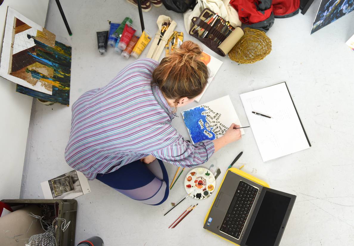 A student sitting on the floor working, surrounded by art supplies