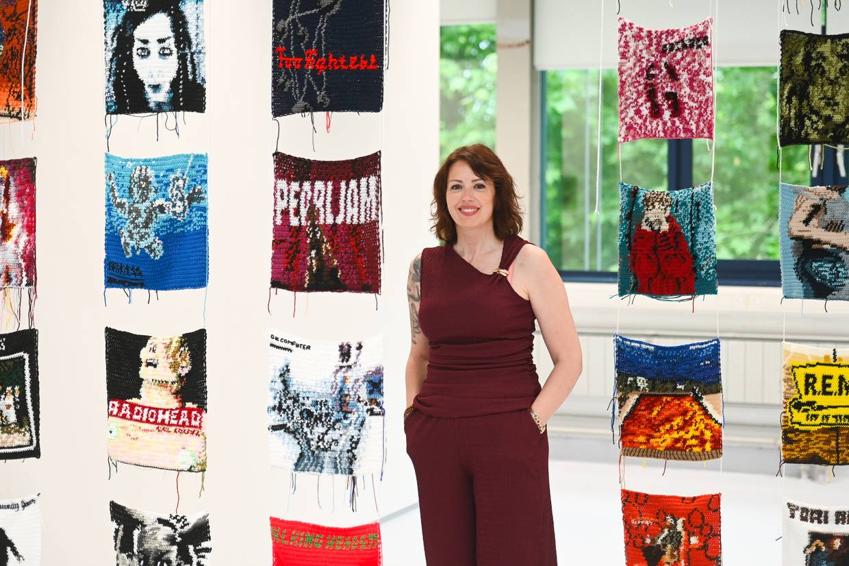 Gemma Upson at the Arts Degree Show with the crocheted album art covers hanging down either side of her