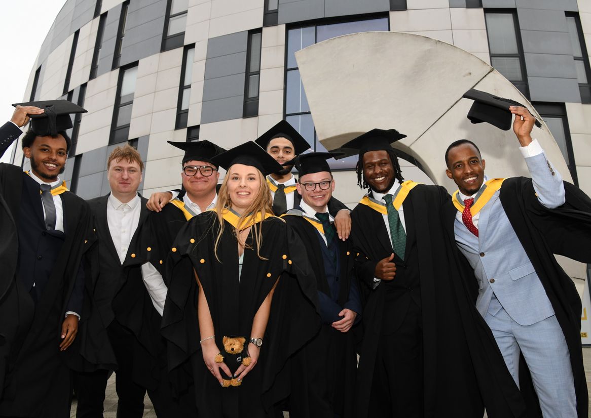 Students gathered by the question mark sculpture dressed in graduation robes