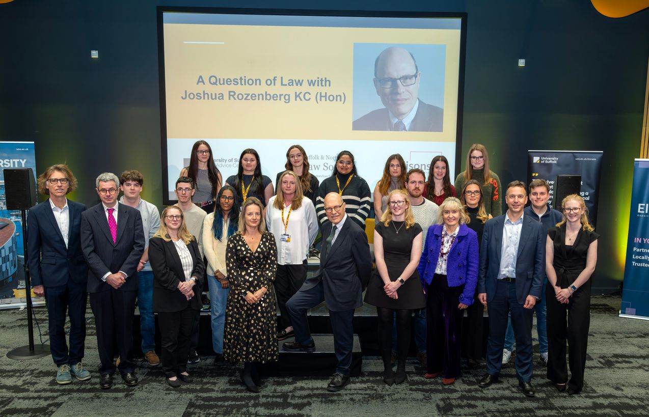 Staff and students from the University of Suffolk with Joshua Rozenberg KC. They are standing in front of the stage for the event