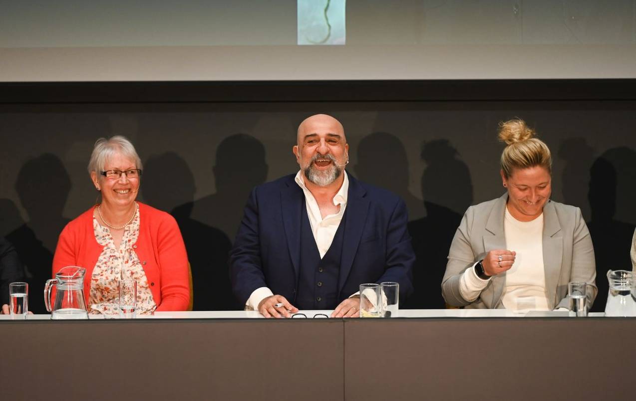 Host Omid Djalili speaking to delegates at the Spotlight Suffolk event, seated to his right is Prof Helen Langton and to his left is Sophie Alexander-Parker