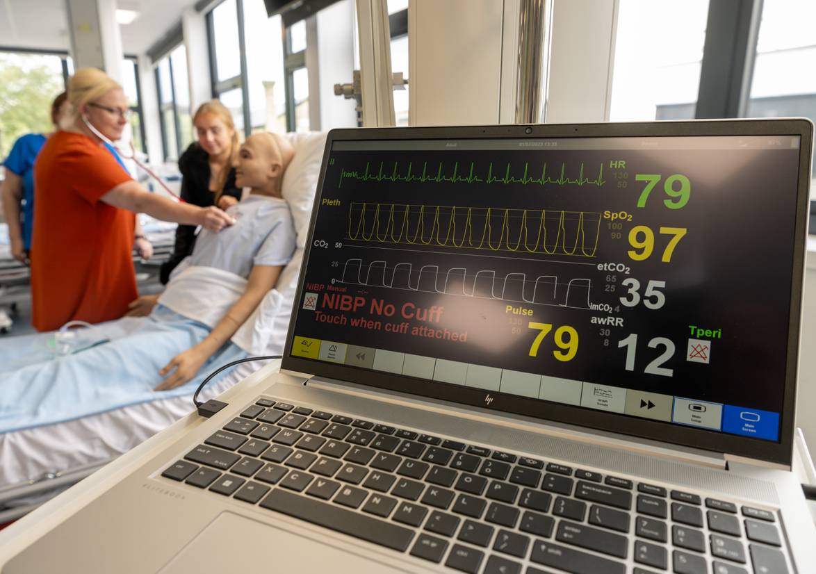 Close-up of a laptop with student listening to heart rate in the background