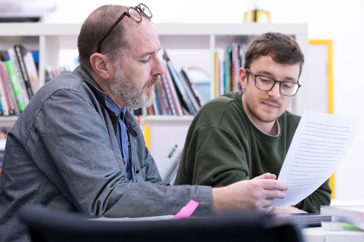 A lecturer sitting with a student discussing their work
