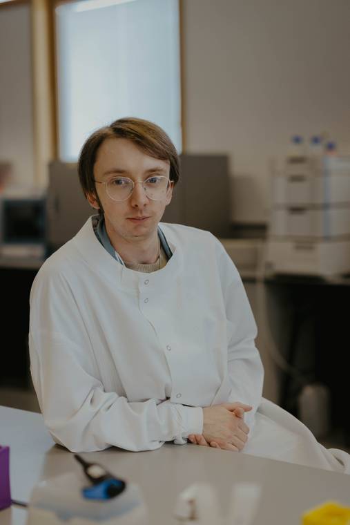 A graduate sat in a science lab wearing a white lab coat