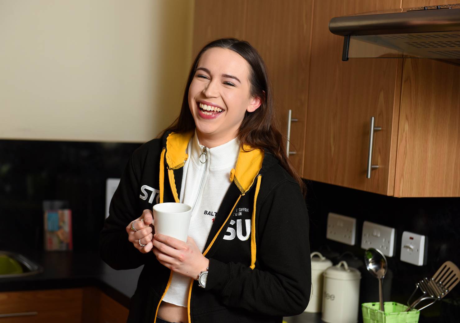 A student smiling and holding a mug in a kitchen