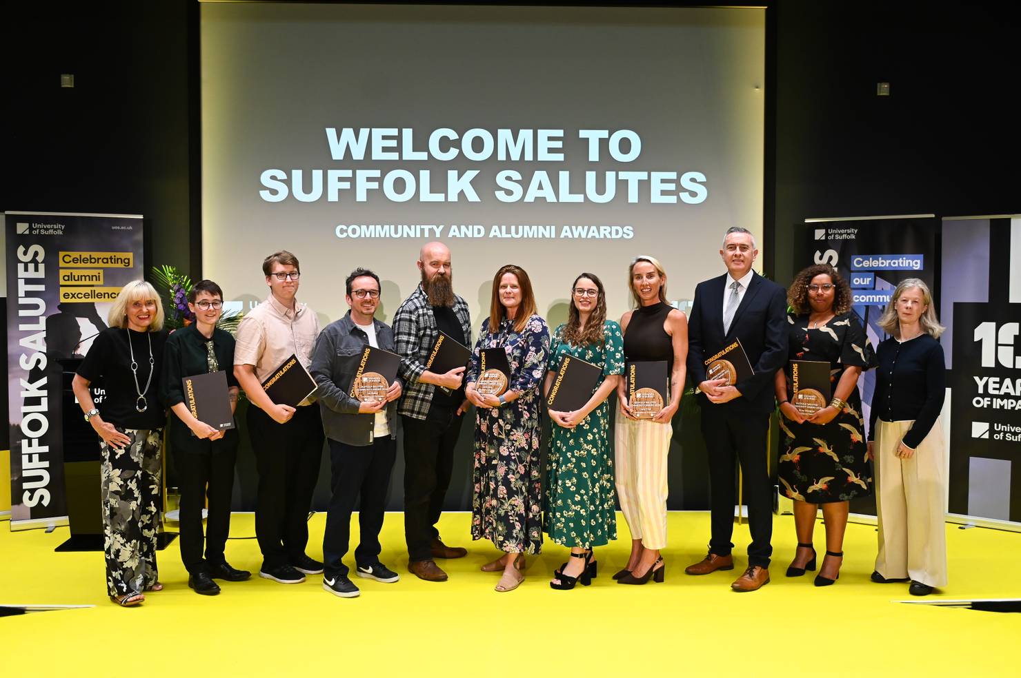 Winners of the Alumni Award and Community Award at the Suffolk Salutes 2026 event, standing on stage and holding their awards