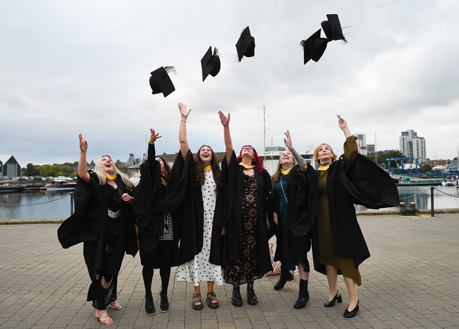 Students dressed in graduation robes lined up on Ipswich waterfront and tossing their caps in the air in celebration