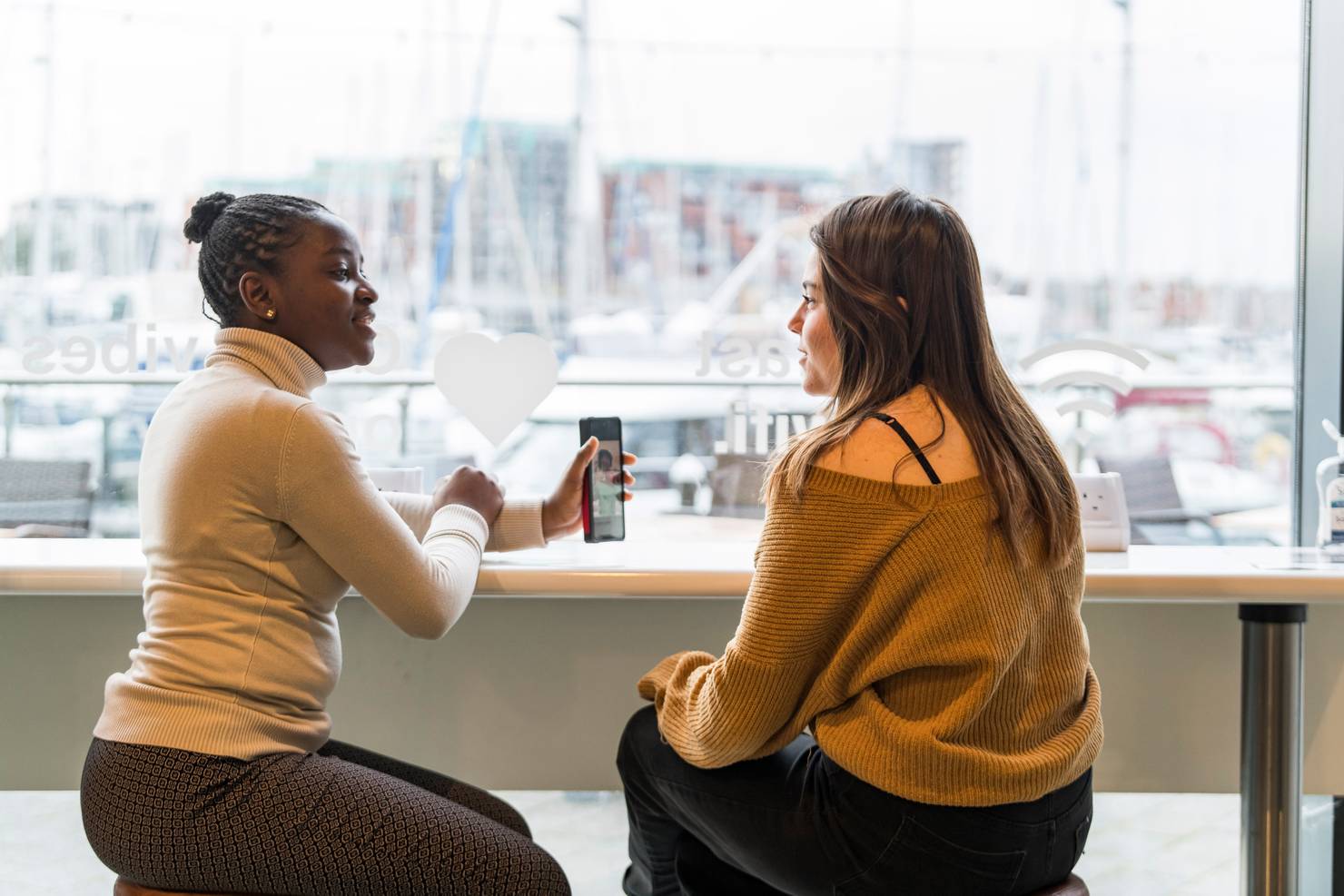 Two student sitting in a cafe looking at a mobile phone