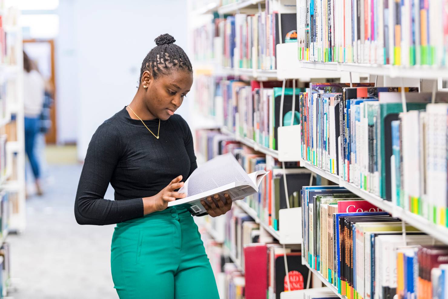 A student reading a book in front of a bookshelf