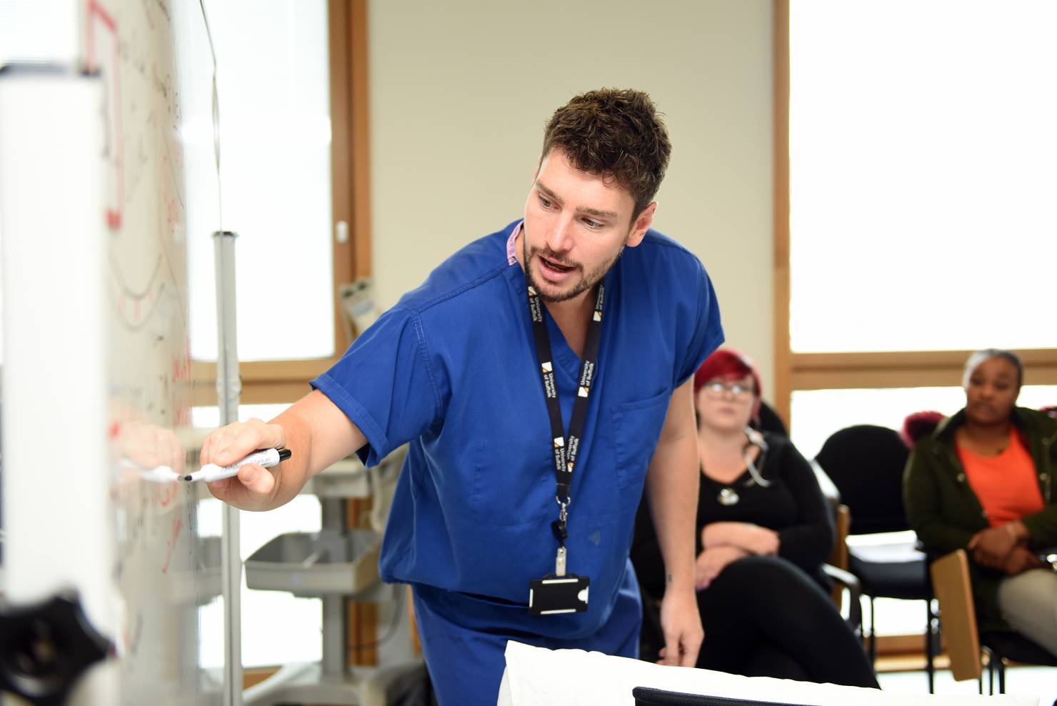 A lecturer drawing on a whiteboard in scrubs