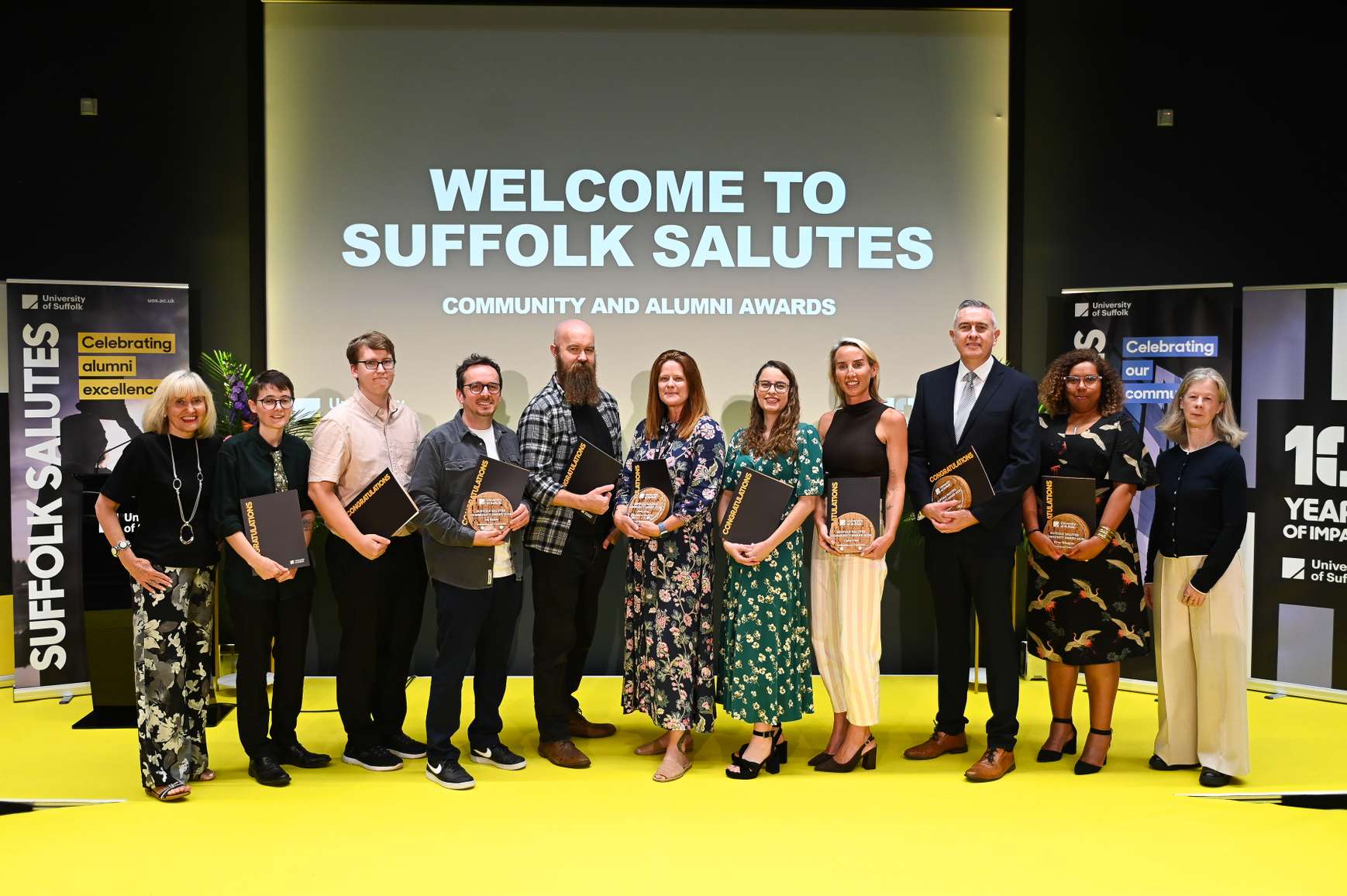 Winners of the Alumni Award and Community Award at the Suffolk Salutes 2026 event, standing on stage and holding their awards