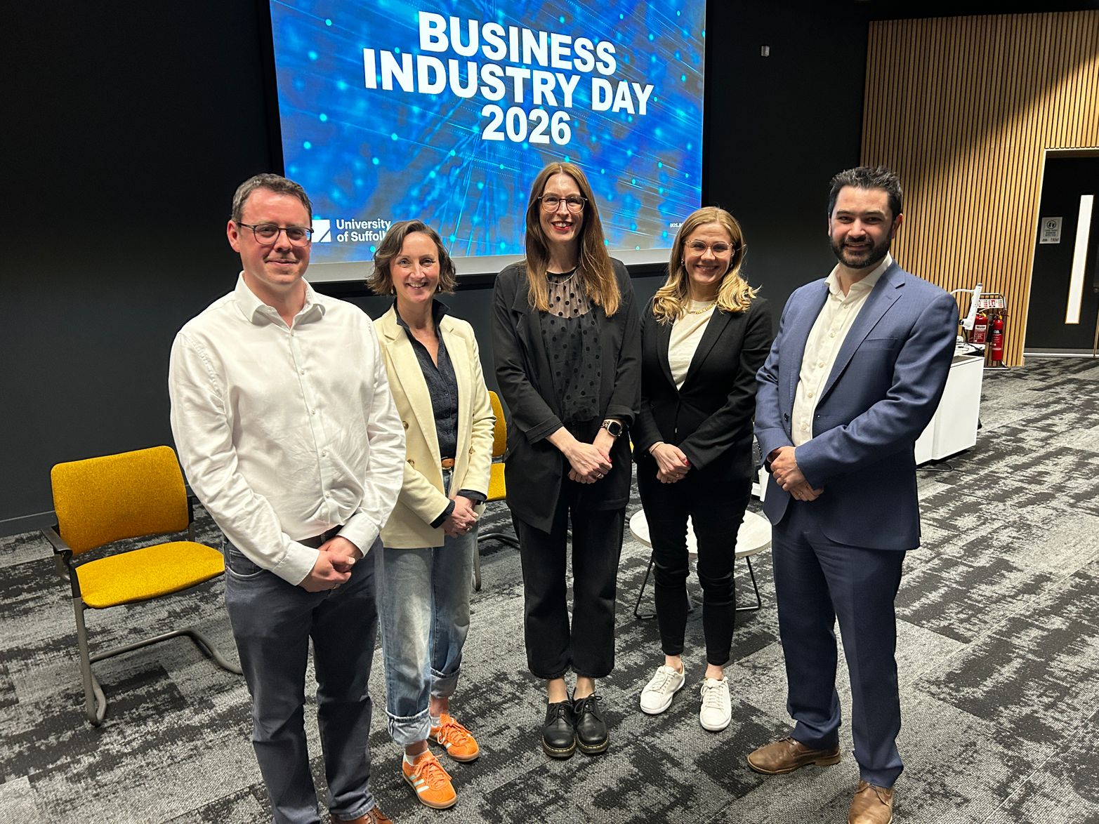 The speakers at the Business Industry Day gathered at the front of The Hold lecture theatre, with the words 'Business Industry Day' on the screen behind. left to right: Derek Holmes, C-J Green, Claire Culley, Shelby Flora and Tom Cole