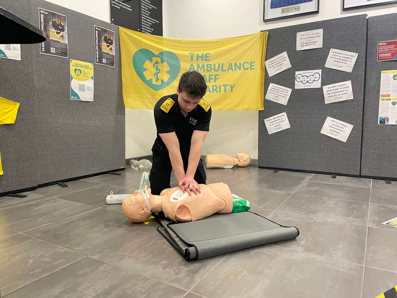 A student kneeling on the floor and completing chest compressions on a mannequin