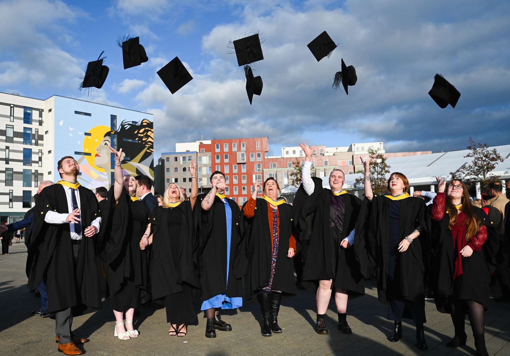 Students at the 2024 graduation ceremonies standing outside on the waterfront and tossing their mortar board hats into the air in celebration