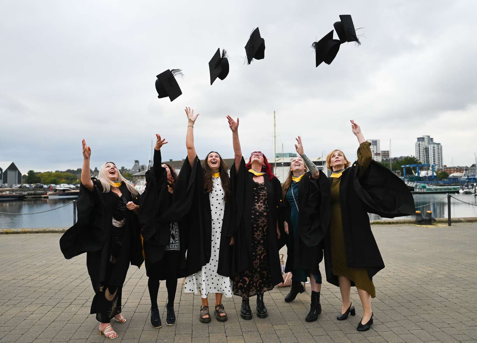 Students dressed in graduation robes lined up on Ipswich waterfront and tossing their caps in the air in celebration