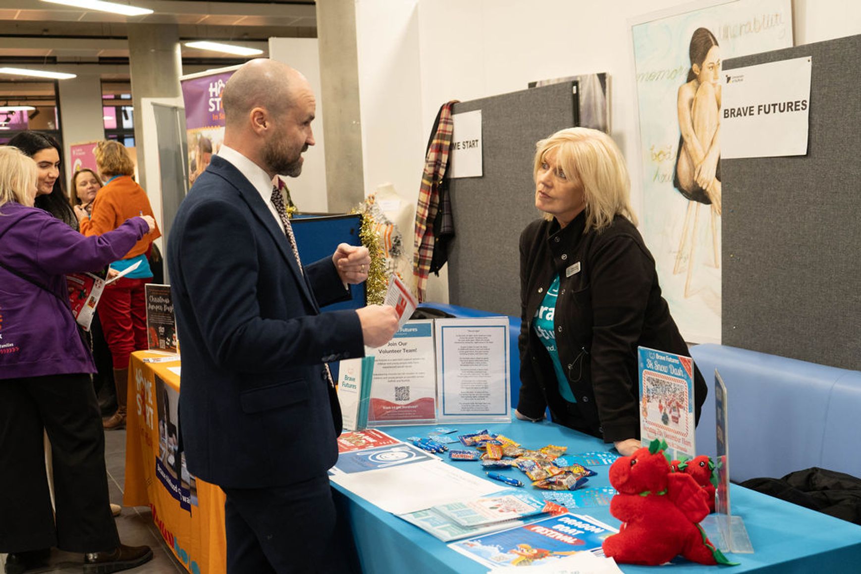 A representative from Brave Futures standing behind a stall at the Gift of Christmas event. She is speaking with someone at the stall