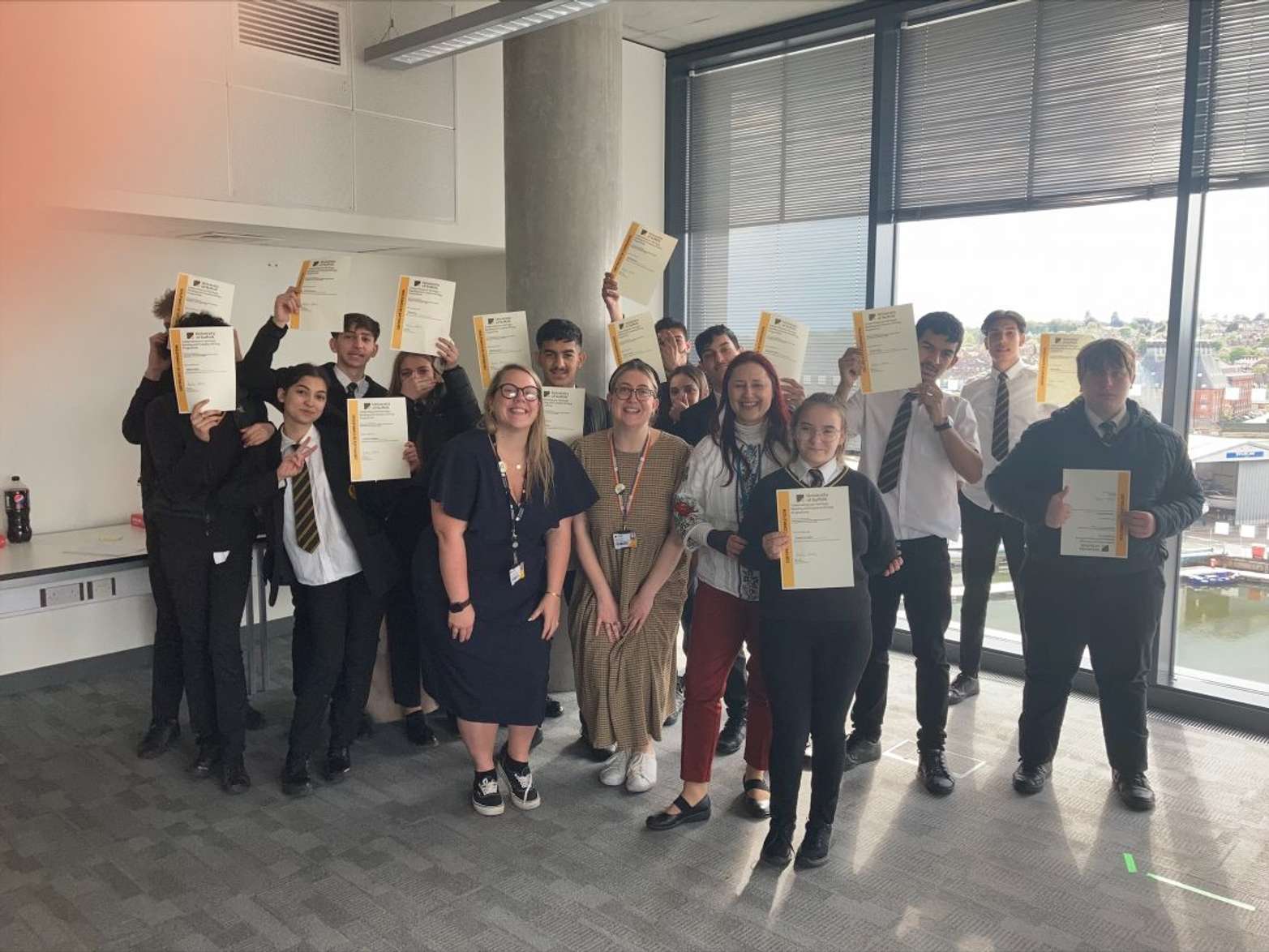 Roma students from Stoke High School with University of Suffolk staff at the Waterfront campus. They are smiling and holding certificates.