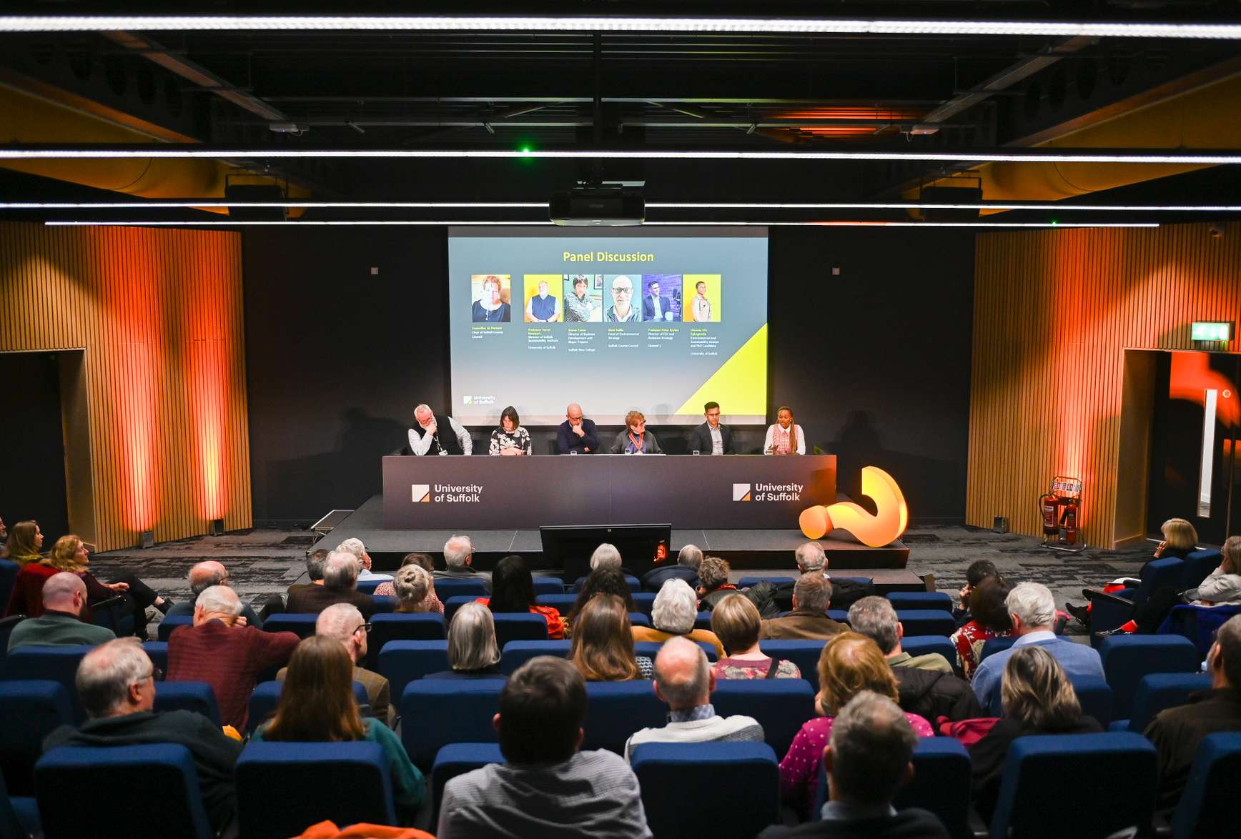 A previous Spotlight Suffolk event. The audience in a lecture theatre are listening to a panel of speakers seated at a front desk