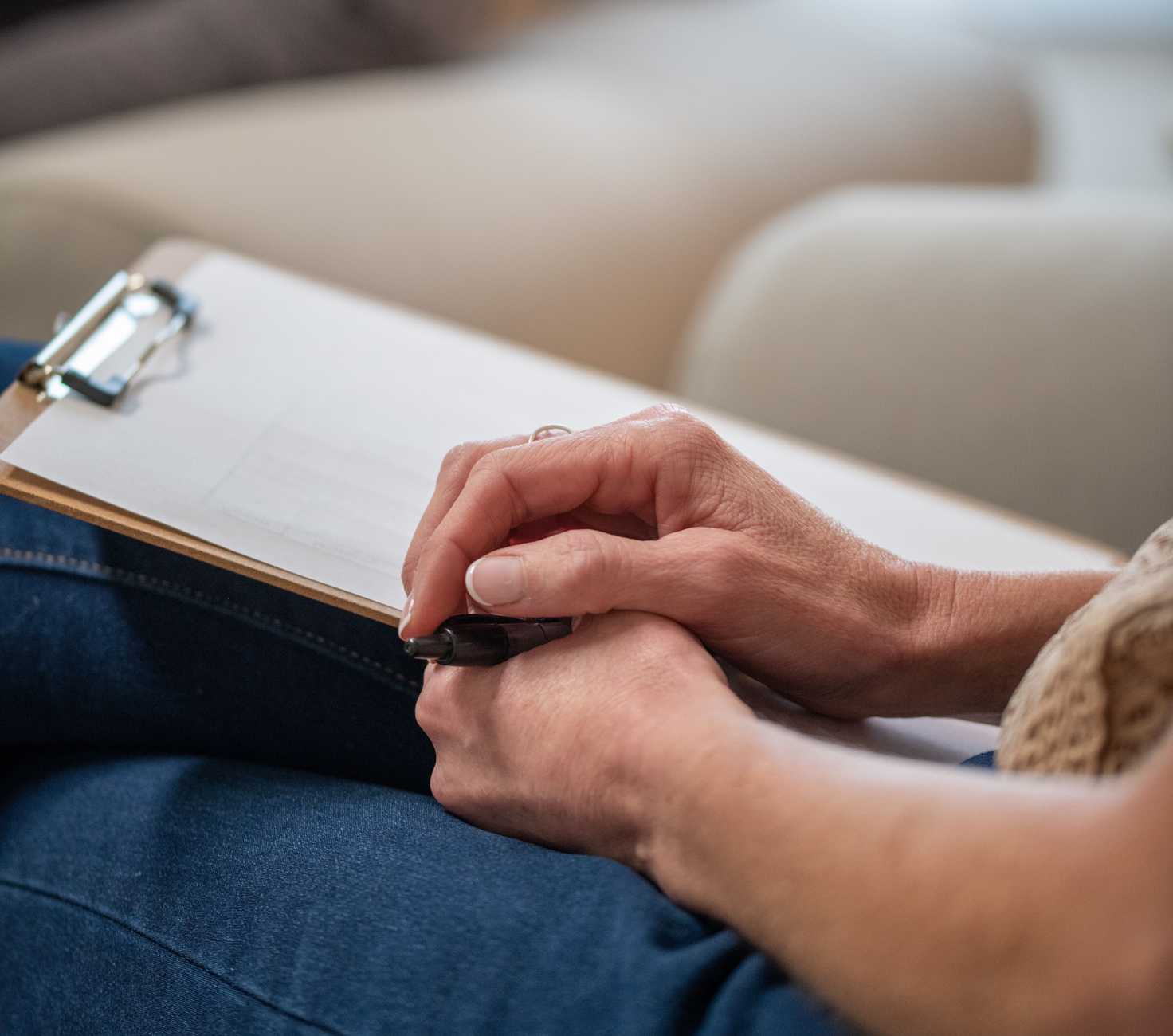 A close-up image of hands holding a pen and a clipboard, taking notes from someone in a counselling session