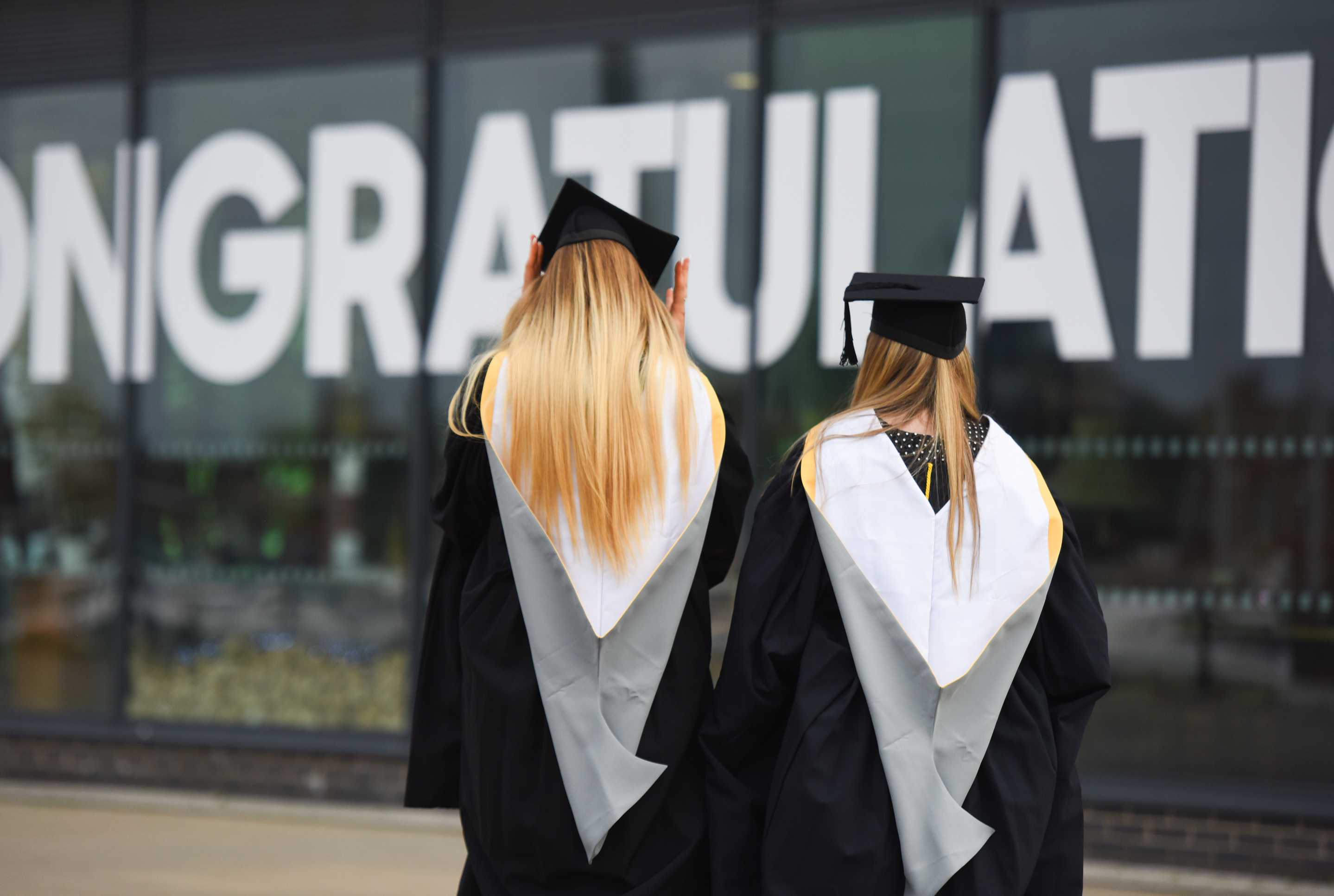 The backs of two students standing in their caps and gowns