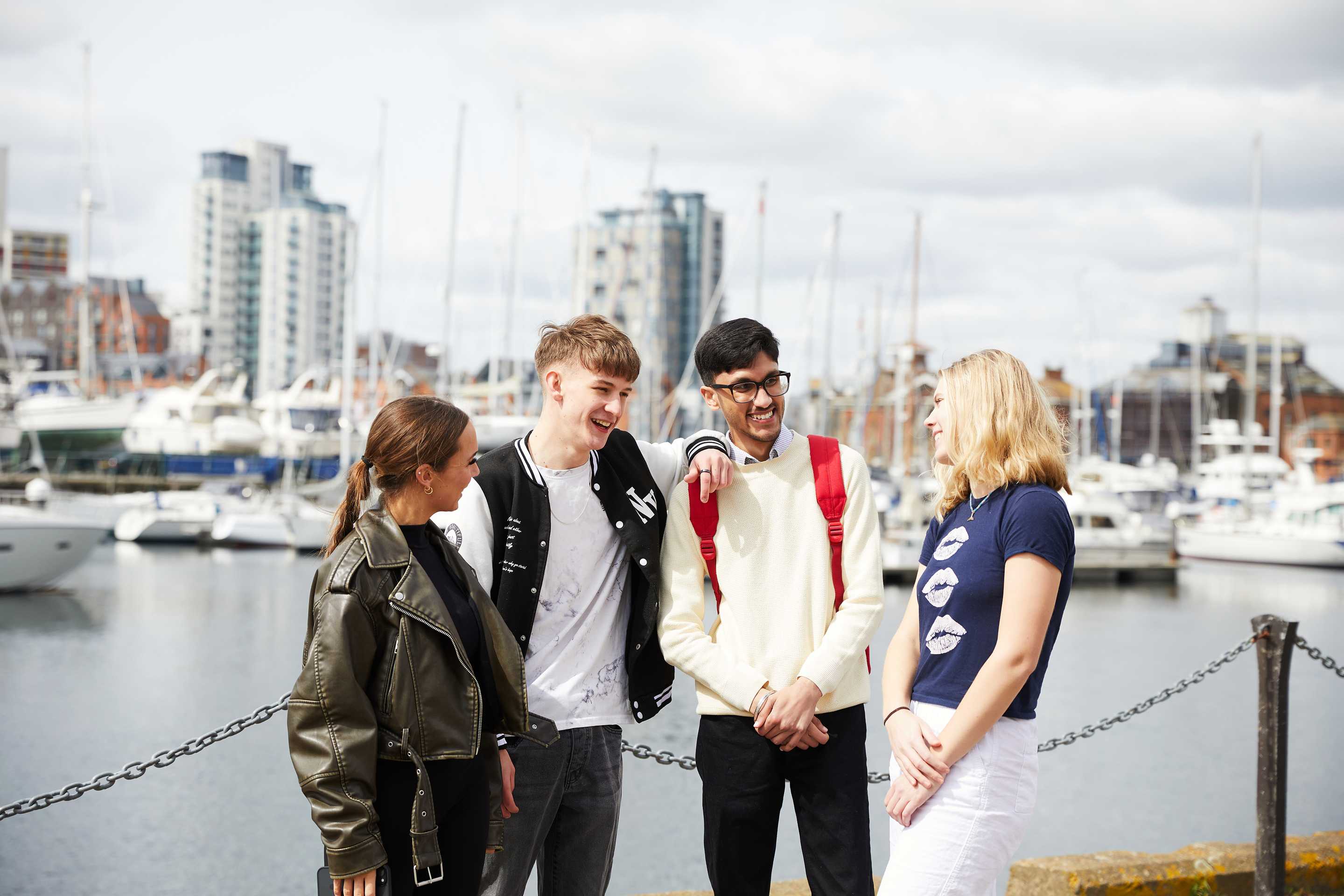 A group of four students chatting outside on Ipswich Waterfront. They are laughing and smiling