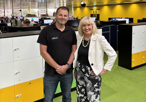 Halo Chief Executive Paul Hamilton (left) and University of Suffolk Vice-Chancellor Jenny Higham standing side by side in Halo's offices, with Halo staff working in the background