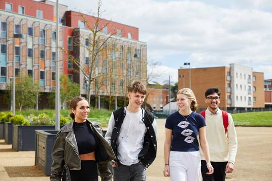 Four students walking all the Waterfront with Athena Hall halls of residence visible behind. The students are chatting and laughing