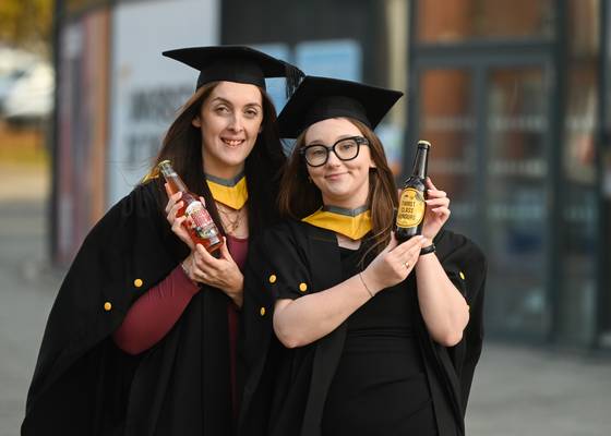 Business Management graduates Adele Harris (left) and Rebecca Mines dressed in their graduation robes and holding the brews they designed and made by Humber Doucy Brewing Company