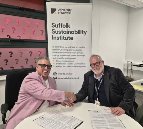 Dr Jehan Kanga from Rux Energy and Professor Darryl Newport seated at a table shaking hands. In front of them on the table is the memorandum of understanding they have signed, and the Suffolk Sustainability Institute banner behind