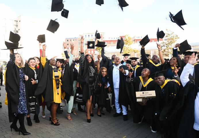 Graduates dressed in graduation robes throwing their mortar board hats into the air on Ipswich Waterfront