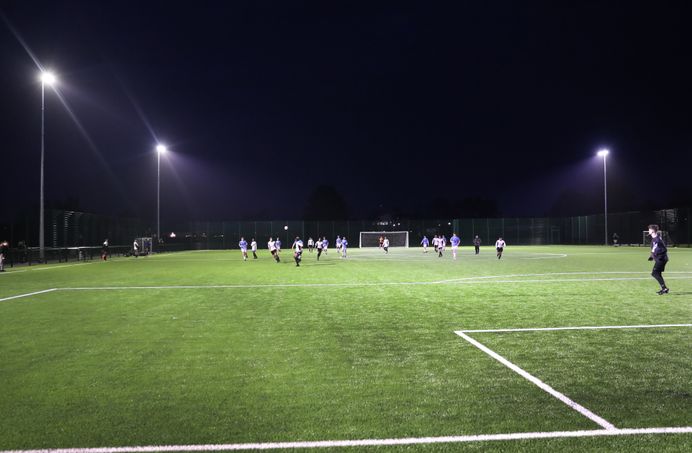 A wide shot photo of two student football teams playing a game under the floodlights