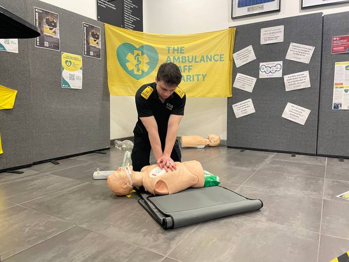 A student kneeling on the floor and completing chest compressions on a mannequin