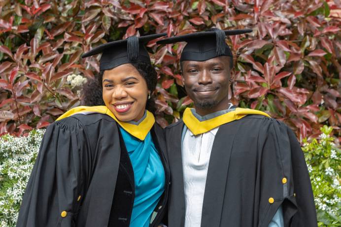 Wife-and-husband Favour Nzube Madu (left) and CHukwuebuka Joshua Madu dressed in graduation robes and smiling