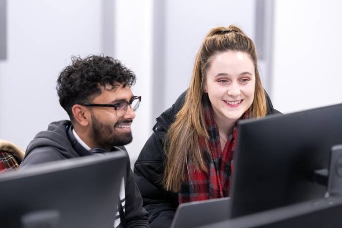 A photo of two students looking at a computer screen and smiling
