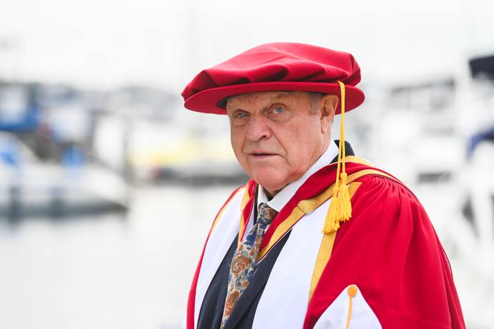 A head and shoulders photo of Charlie Haylock standing on the Waterfront, dressed in graduation robes