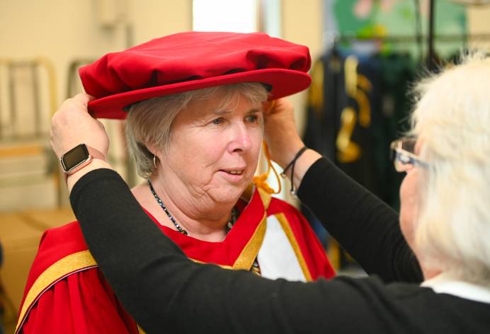 Cathy Ryan dressed in graduation robes having her hat adjusted