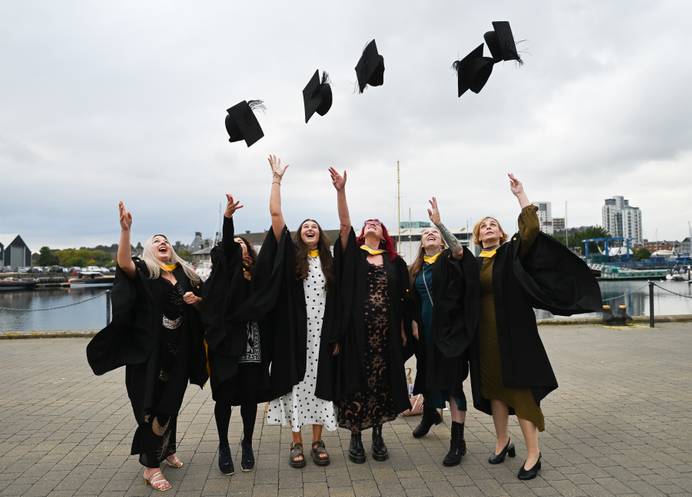 Students dressed in graduation robes lined up on Ipswich waterfront and tossing their caps in the air in celebration