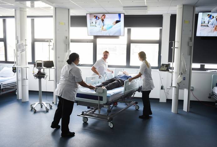 A photo of three students wheeling a hospital bed in the University simulation ward