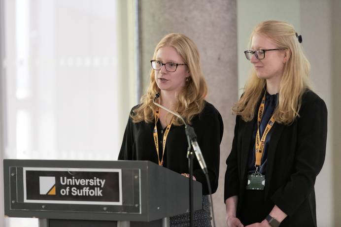 Two students from the University of Suffolk legal Advice Centre speaking at a podium for an event