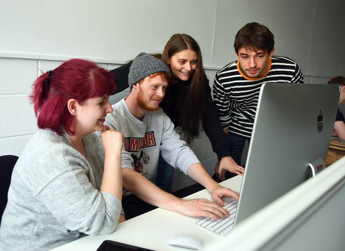 A photo of several students gathered around a computer screen and making suggestions