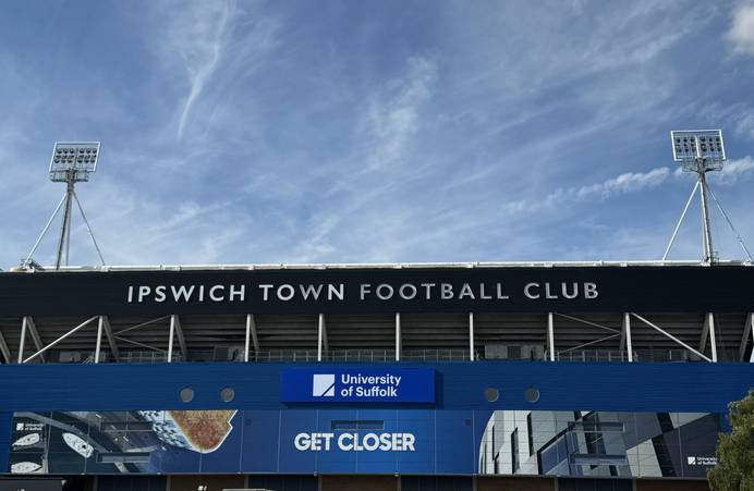 The outside of Portman Road stadium with the words 'Ipswich Town Football Club' visible. Beneath are the University of Suffolk logo, image of the Waterfront Building and the words 'Get Closer'