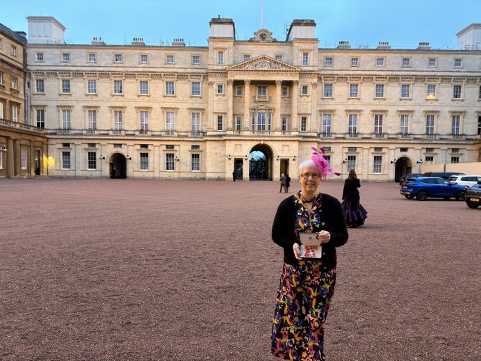 A photo of Prof Helen Langton standing outside Buckingham Palace holding her MBE