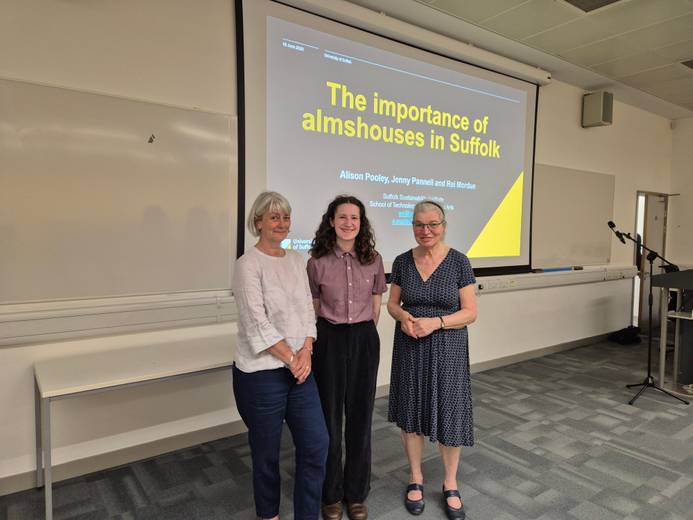 three women standing in front of a display screen in a university lecture theatre
