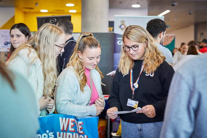 New students enjoying the Freshers Fair, talking to a staff member with stalls in the background