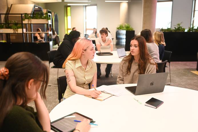 Students seated around a table in the Library, chatting through some group work