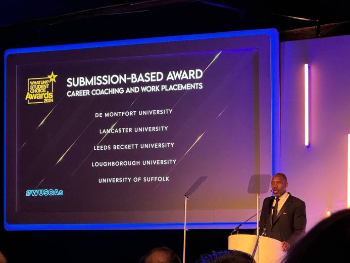 Lenny Henry presenting the What Uni? Student Choice Awards. The names of the universities in the Submission Category, including Suffolk, are listed on the screen behind