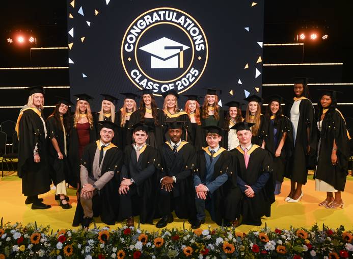 The first graduating Physiotherapy students dressed in their graduation robes and standing on the stage