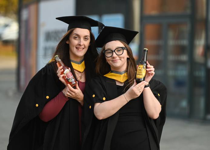 Business Management graduates Adele Harris (left) and Rebecca Mines dressed in their graduation robes and holding the brews they designed and made by Humber Doucy Brewing Company