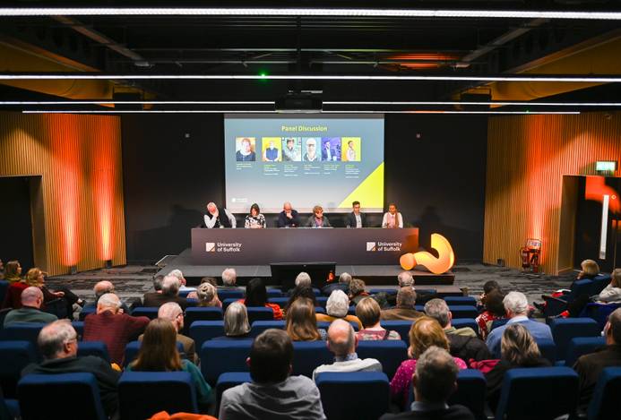 A previous Spotlight Suffolk event. The audience in a lecture theatre are listening to a panel of speakers seated at a front desk