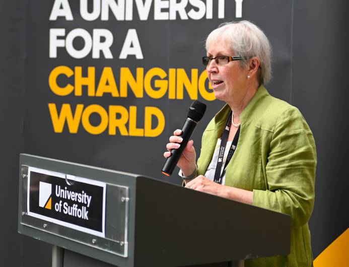 Prof Helen langton holding a microphone and speaking, The backdrop banner says 'a university for a changing world'